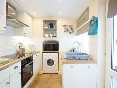 A kitchen with white cabinets a washing machine a microwave a stovetop and a sink at Old Post Office in Bull Bay