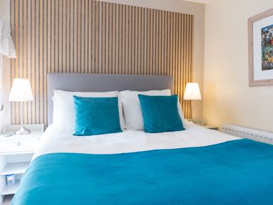 A bedroom with a bed with teal pillows and a teal blanket and two bedside tables with lamps at Old Post Office in Bull Bay