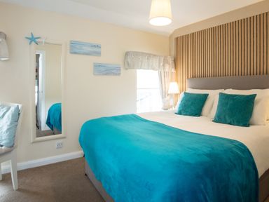 A bedroom with a double bed with teal blankets and pillows a lamp and a mirror on the wall at Old Post Office in Bull Bay