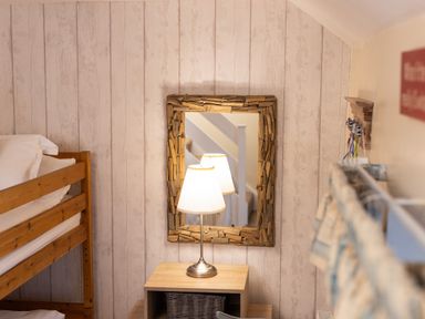 A bedroom with a wooden bunk bed a table lamp on a wooden nightstand and a mirror with a wooden frame at Old Post Office in Bull Bay
