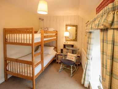 A bedroom with wooden bunk beds a rocking chair a desk with a lamp and a mirror at Old Post Office in Bull Bay