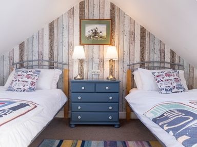 A bedroom with two single beds separated by a blue chest of drawers and two table lamps at Old Post Office in Bull Bay