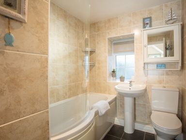 A bathroom with a bathtub shower combination sink toilet and small window at The Old Post Office in Bull Bay
