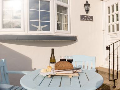 A small outdoor table with two chairs bread cheese wine bottle and two glasses at The Old Post Office in Bull Bay