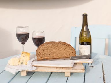 A table with a loaf of bread, two glasses of red wine, two pieces of cheese, a knife, a cutting board, and a bottle of wine at Old Post Office in Bull Bay
