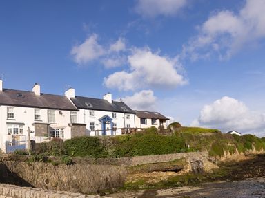 A row of houses with stone walls and green bushes near a rocky shoreline at Old Post Office in Bull Bay