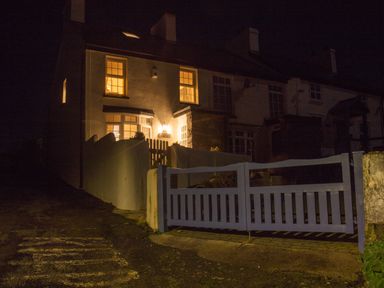 A lit house with glowing windows and a closed wooden gate at night at Old Post Office in Bull Bay