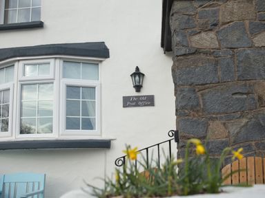 A white house exterior with a window a light fixture a sign that says The Old Post Office and stone walls at Old Post Office in Bull Bay