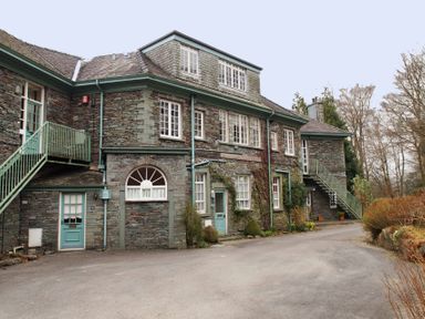 A stone building with teal doors and stairs surrounded by bushes and trees at Sethera in Ambleside
