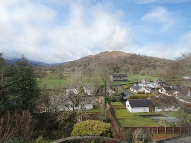 A rural village with houses a stone barn green fields and a wooded hill in the background at Sethera in Ambleside