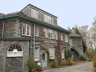 A stone building with multiple windows green doors and an external metal staircase surrounded by plants and trees at Sethera in Ambleside