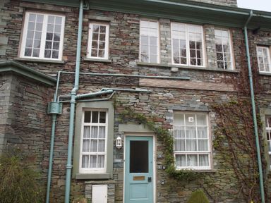 The stone exterior of a building with multiple white-framed windows and a blue door with climbing plants at Sethera in Ambleside