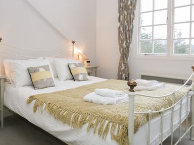 A bedroom with a bed made with white sheets two grey and yellow pillows a beige knitted throw a window and grey patterned curtains at Sethera in Ambleside
