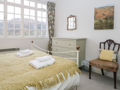 A bedroom with a bed covered with a yellow blanket and white towels on top next to a dresser with a mirror above and a wooden chair with a cushion at Sethera Ambleside