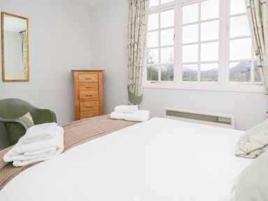 A bedroom with a bed towels on it a green chair wooden chest of drawers and a window with curtains at Sethera in Ambleside
