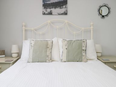A bedroom with a white metal bed frame green and floral pillows bedside tables with lamps and a round wall mirror at Sethera in Ambleside