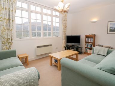 A living room with two sofas a wooden coffee table a television on a stand and a bookshelf at Sethera in Ambleside