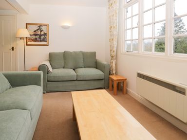 A sitting room with two green sofas a wooden coffee table a floor lamp and windows at Sethera in Ambleside