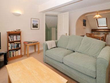 A living room with a green sofa a wooden coffee table a bookshelf and a dining area at Sethera in Ambleside