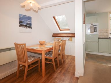 A dining area with a wooden table and four chairs near a skylight window adjacent to a kitchen at Sethera in Ambleside