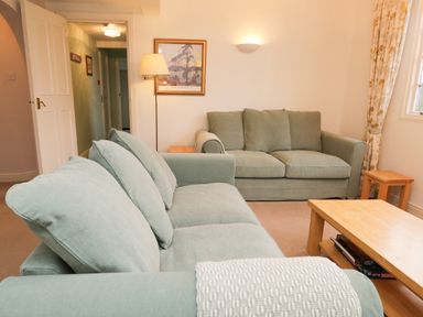 A living room with two green sofas a wooden coffee table and side tables a floor lamp and a framed picture on the wall at Sethera in Ambleside