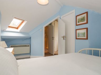 A bedroom with a bed white bedding skylight window heater and two framed pictures on blue walls at Sethera in Ambleside