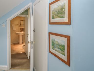 A hallway with two framed landscape paintings on a blue wall and a partially open door leading to a bathroom at Sethera in Ambleside