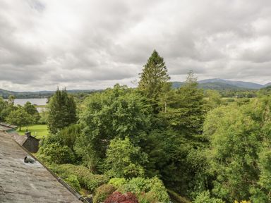 A view of trees hills and a lake with a stone roof in the foreground at Sethera in Ambleside
