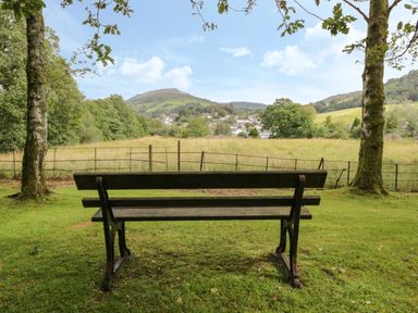 A wooden bench between two trees facing a field with hills and a village in the background at Sethera in Ambleside
