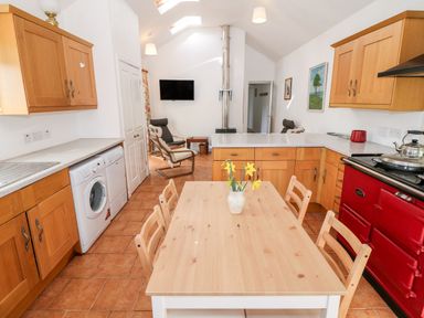 A kitchen with wooden cabinets a dining table with chairs and a red stove at Y Buarth in Waunfawr