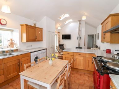 A kitchen with wooden cabinets a dining table with chairs and a red stove at Y Buarth in Waunfawr