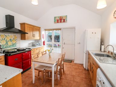 A kitchen with wooden cabinets red stove wooden dining table with chairs and a white refrigerator at Y Buarth in Waunfawr