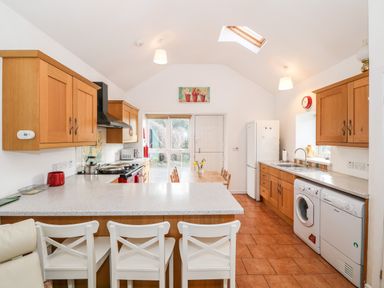 A kitchen with wooden cabinets white appliances and a countertop with white chairs at Y Buarth in Waunfawr