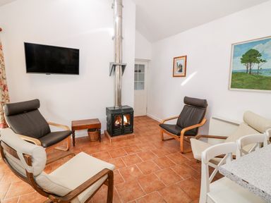 A sitting room with four armchairs a small wooden table a wood burning stove and a wall mounted television at Y Buarth in Waunfawr
