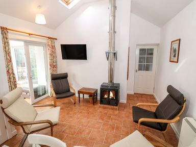 A sitting room with armchairs a wood burning stove a wall mounted tv and sliding glass doors at Y Buarth in Waunfawr