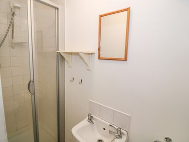A bathroom with a shower cabin a sink with taps a wooden framed mirror and a wall shelf at Y Buarth in Waunfawr