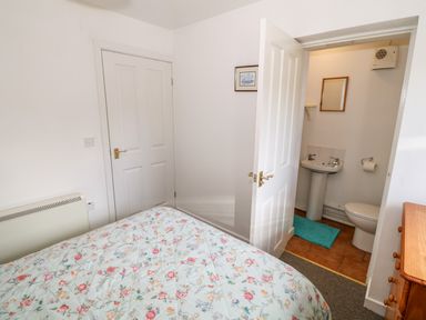 A bedroom with a bed covered in floral bedding a door leading to a bathroom with a sink and toilet at Y Buarth in Waunfawr