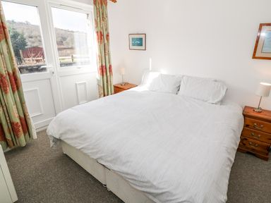 A bedroom with a double bed white bedding wooden bedside tables lamps and doors with curtains at Y Buarth in Waunfawr