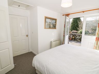 A bedroom with a bed a door to an outside patio a framed picture on the wall and curtains at Y Buarth in Waunfawr