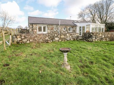 A stone house with a grass lawn and a bird bath in front at Y Buarth in Waunfawr
