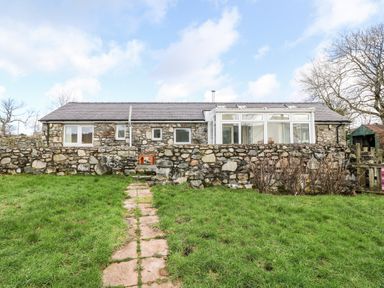 A stone house with a tiled roof and a stone wall in front with a grass path leading to it at Y Buarth in Waunfawr