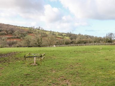 A grassy field with a wooden fenced post and a stone wall in the background surrounded by hills at Y Buarth in Waunfawr