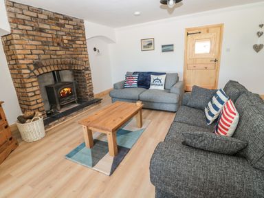 A living room with two sofas a wooden coffee table a brick fireplace and a wooden door at 24 Hauxley Links in Low Hauxley near Amble
