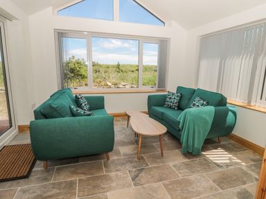 A seating area with two green sofas and a wooden coffee table in a room with large windows at 24 Hauxley Links in Low Hauxley near Amble