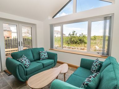 A sitting area with two teal sofas and patterned cushions around a wooden coffee table by large windows at 24 Hauxley Links in Low Hauxley near Amble