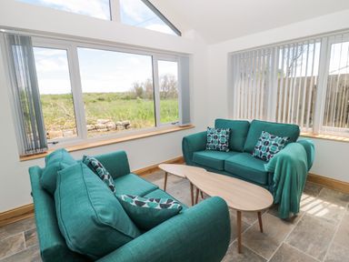 A room with teal sofas and patterned cushions around two wooden coffee tables at 24 Hauxley Links in Low Hauxley near Amble