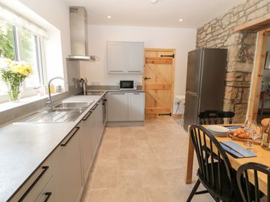A kitchen with gray cabinets a stainless steel refrigerator and a wooden dining table with black chairs at 24 Hauxley Links in Low Hauxley near Amble