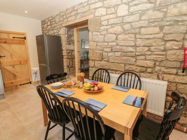 A dining table with black chairs and fruit bowl against a stone wall in a kitchen at 24 Hauxley Links in Low Hauxley near Amble