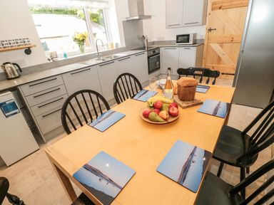 A kitchen with a wooden dining table set with placemats fruit and bread and cabinets with appliances at 24 Hauxley Links in Low Hauxley near Amble