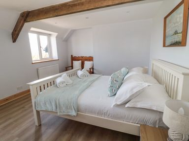 A bedroom with a white bed with pillows and rolled towels a wooden chair by the window and a painting on the wall at 24 Hauxley Links in Low Hauxley near Amble